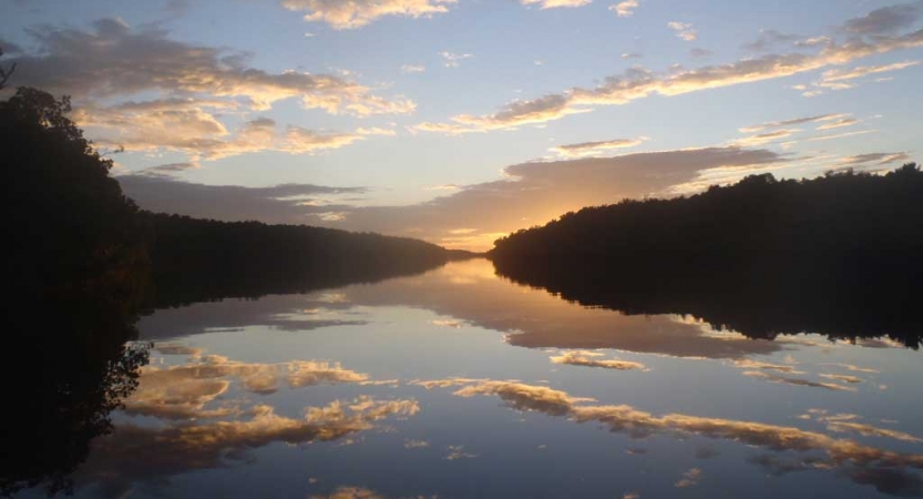 The sky is reflected in a calm body of water framed by trees.